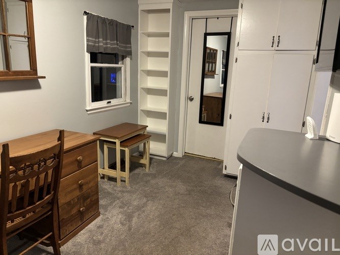 A room with a wooden chair, a desk, and a window with a grey curtain.