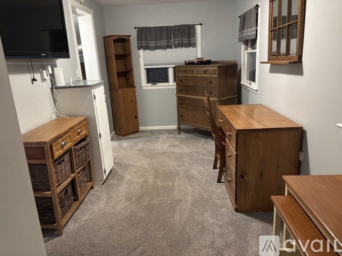 A room with a television, a desk, and a window with curtains.