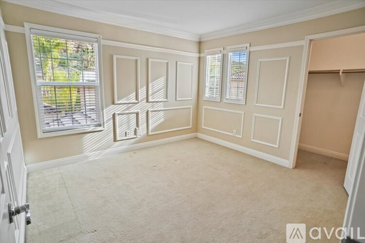 A room with a carpeted floor, a window with blinds, and a door.