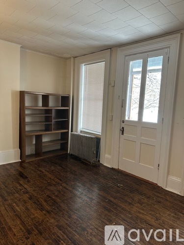 A room with a wooden floor, a white door, and a window with blinds.