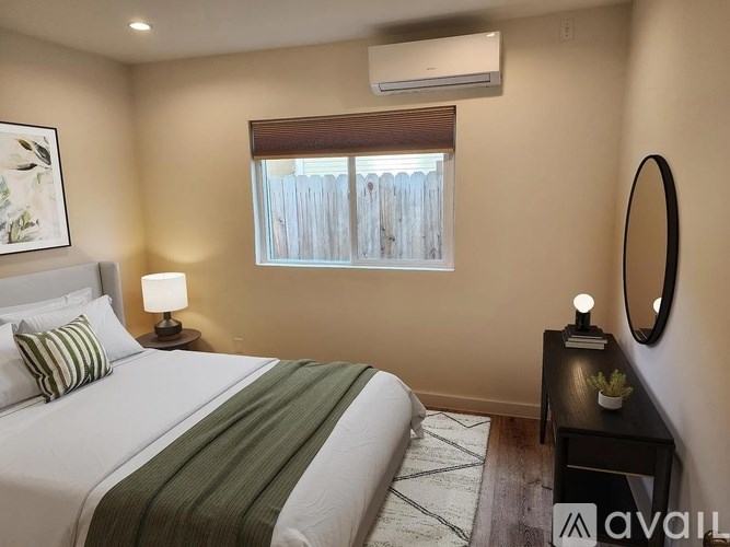 A bedroom with a large bed, a nightstand with a lamp, and a window with blinds.