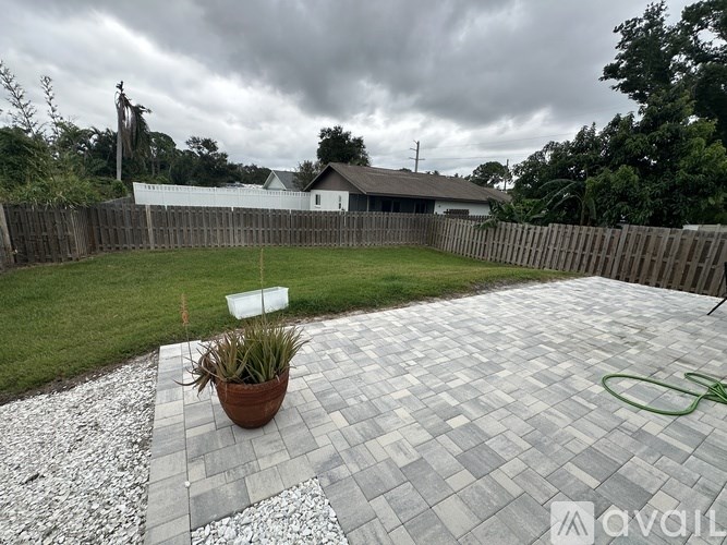 A backyard with a paved area, a plant, and a fence.