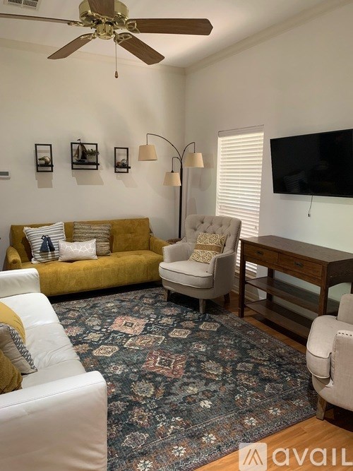 A living room with a yellow couch, a white armchair, and a rug with a pattern on it.