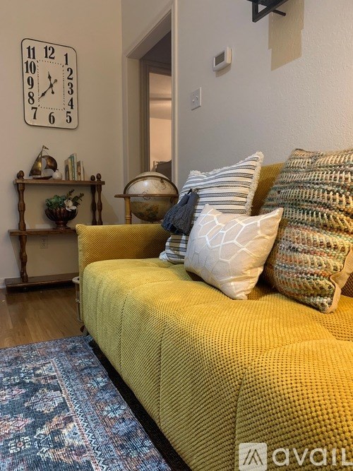 A yellow sofa with a blue rug in front of it and a clock on the wall.