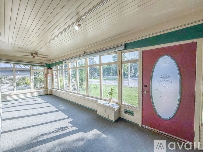 A sunny day in a room with a red door and a bench.