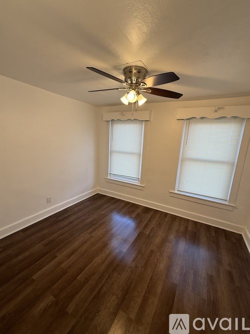 A room with a ceiling fan and two windows.