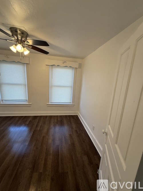 A room with a ceiling fan and two windows.