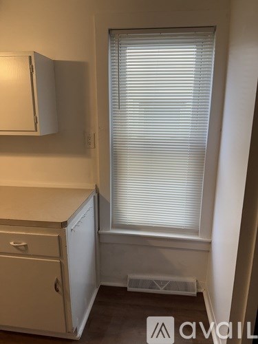 A small kitchen with a white fridge and a window with blinds.