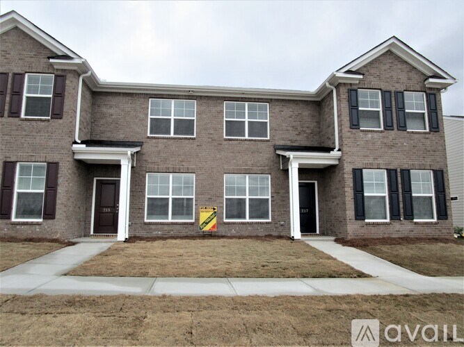 A two-story brick house with a sign in front.