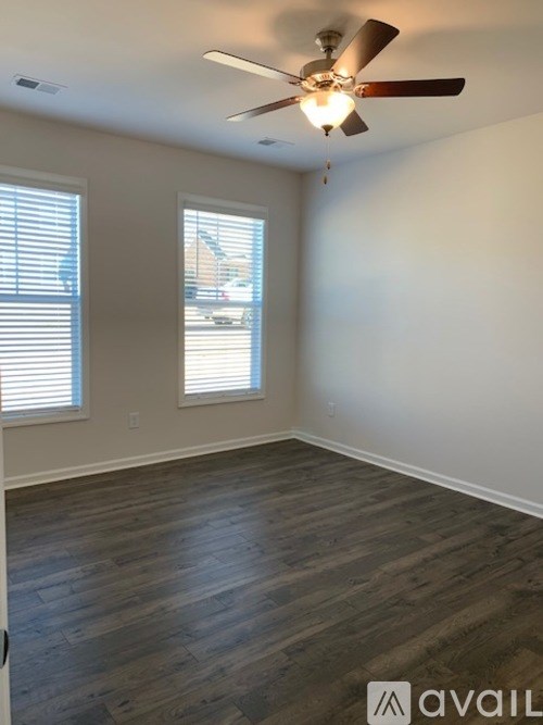 A room with a ceiling fan and two windows.