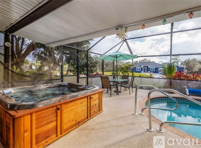 A hot tub is surrounded by chairs and umbrellas in a covered outdoor area.