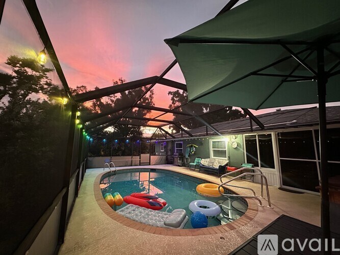 A pool with a sun lounger and a table with chairs is surrounded by a metal fence.
