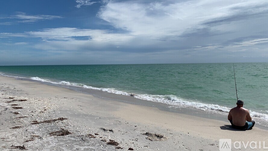 A man is sitting on a beach with a fishing rod.