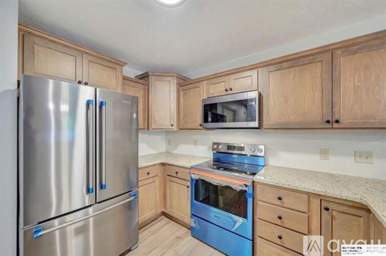 A kitchen with a stainless steel refrigerator, blue oven, and wooden cabinets.
