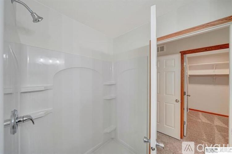 A white bathroom with a shower and a doorway leading to another room.