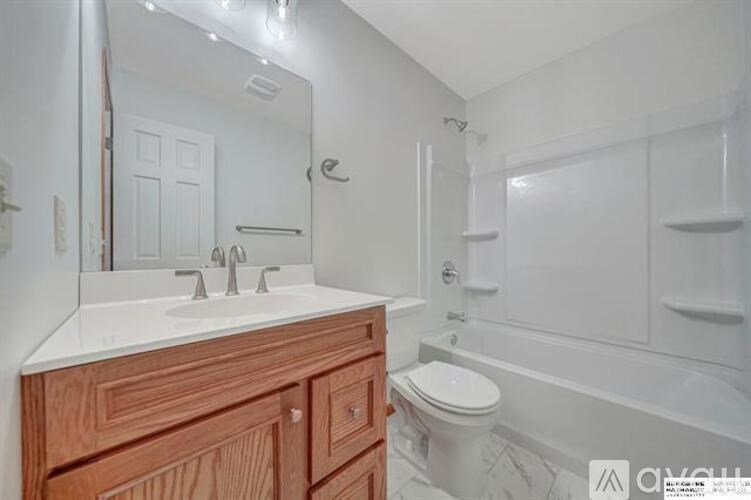 A white bathroom with a wooden vanity and a white toilet.