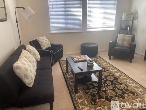 A black couch with white pillows sits in a living room with a rug and a coffee table.