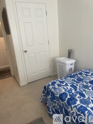 A white door is next to a bed with a blue and white comforter.