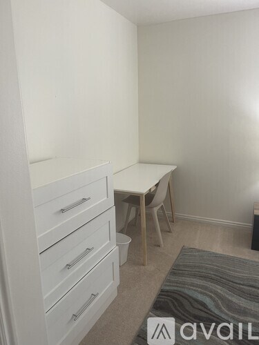 A room with a white table and chairs and a white wardrobe with drawers.