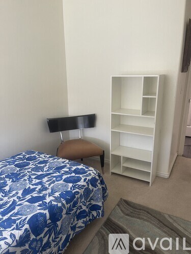A bed with a blue and white comforter sits next to a white shelf unit.