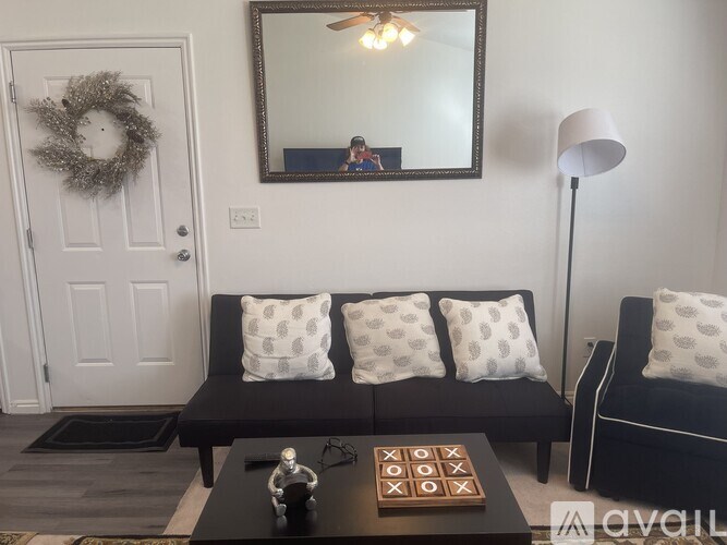 A living room with a black couch, a coffee table, and a mirror on the wall.