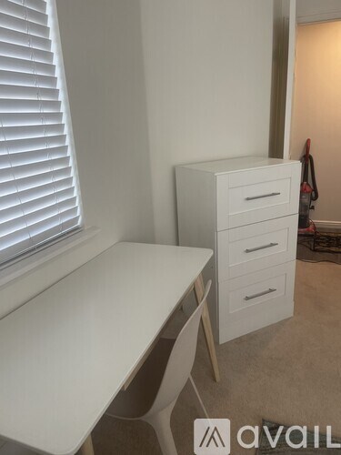 A white desk with a white chair and a white cabinet with three drawers in a room.