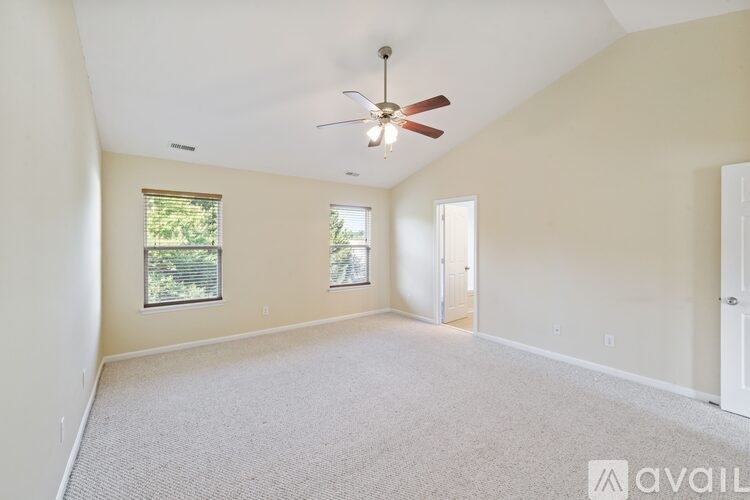 A spacious room with a ceiling fan and two windows.