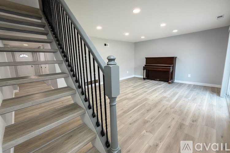 A wooden staircase with a metal railing leads to a room with a wooden floor and a piano.