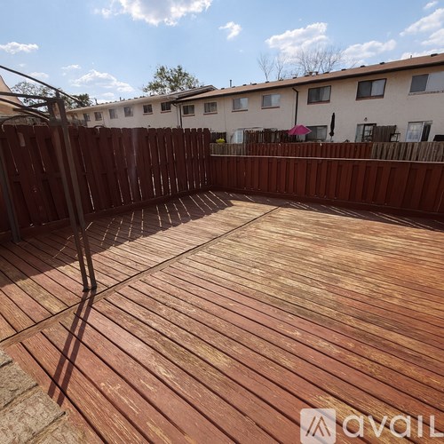 A wooden deck with a railing and a few buildings in the background.