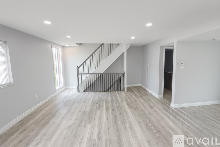 A spacious room with wooden flooring and a staircase with a metal railing.