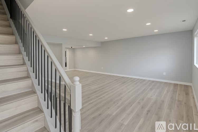 A staircase with wooden steps and white railings leads to a spacious room with light wood flooring and recessed lighting.