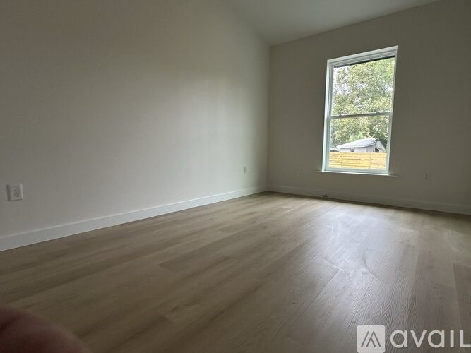 A room with wooden flooring and a window showing a view of a house.