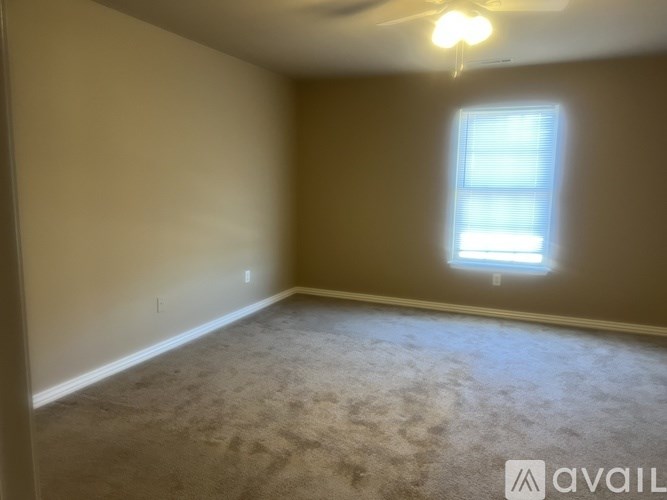 A room with a carpeted floor, a ceiling fan, and a window with blinds.