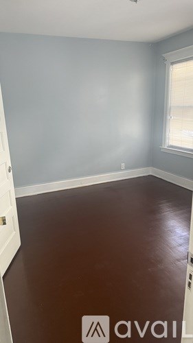 A room with a brown floor and a window with blinds.
