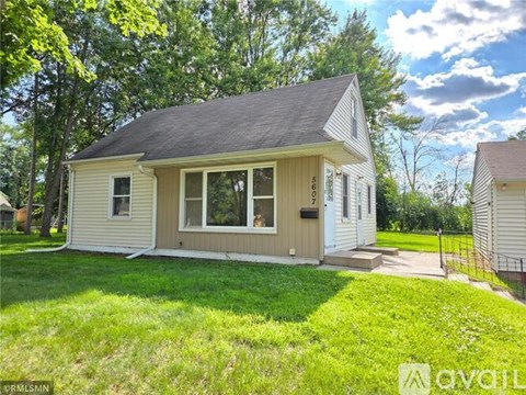A house with a grey roof and a white exterior is surrounded by a grassy area.