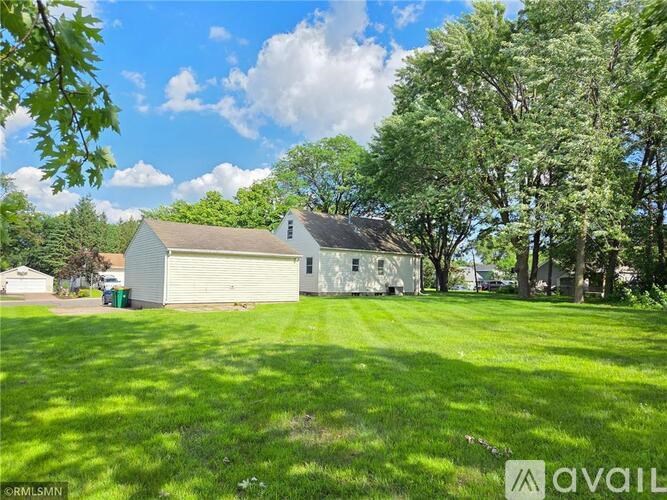 A house with a garage is surrounded by a green lawn and trees.