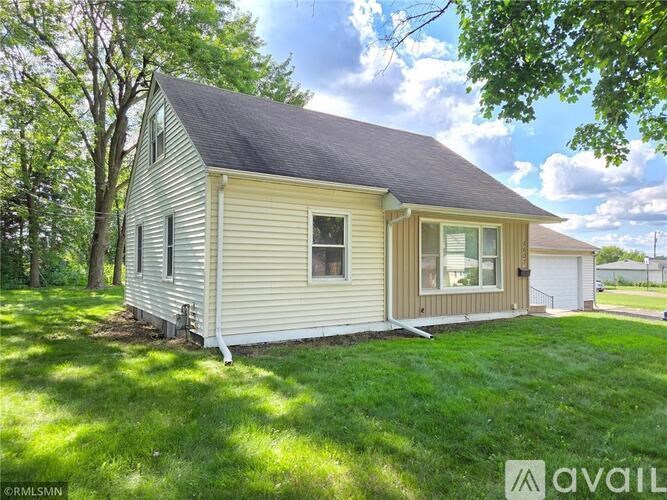 A house with a beige siding and a brown roof is surrounded by green grass.