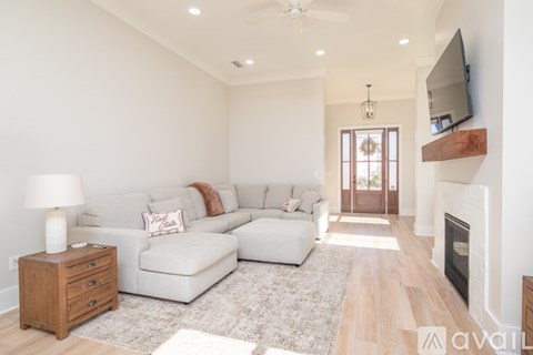 A living room with a white couch, a wooden side table, and a television mounted on the wall.