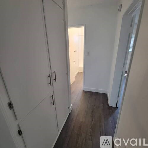 A hallway with white walls and wood flooring.