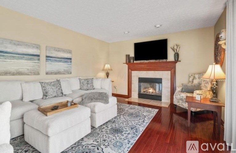 A living room with a white couch, a fireplace, and a TV mounted above it.
