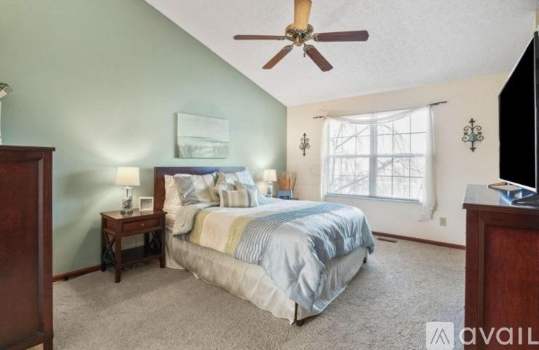 A bedroom with a bed, a ceiling fan, and a window.