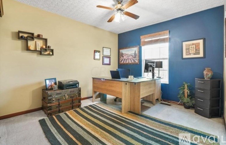 A room with a desk and a ceiling fan.