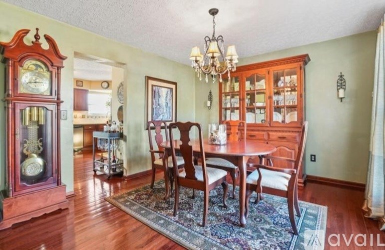 A living room with a wooden table and chairs, a chandelier, and a large clock on the wall.