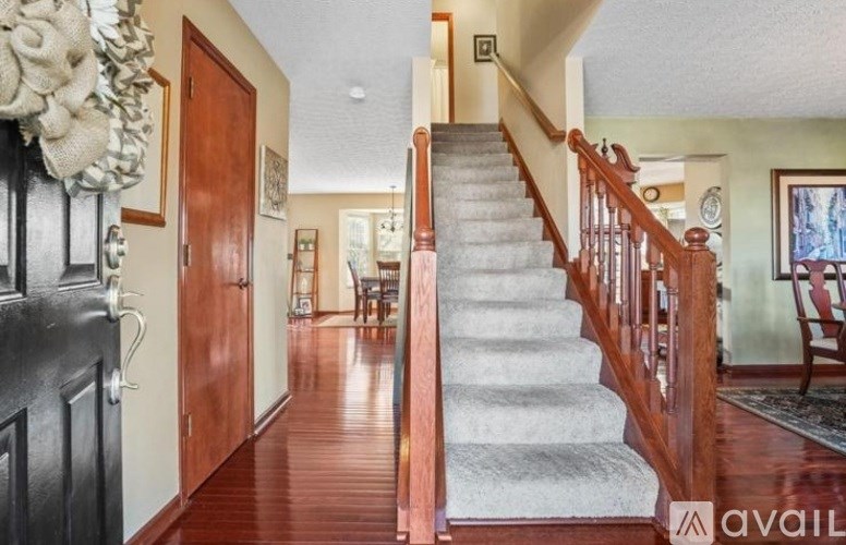 A wooden staircase with a carpeted runner leads up to a landing with a door and a wall hanging.