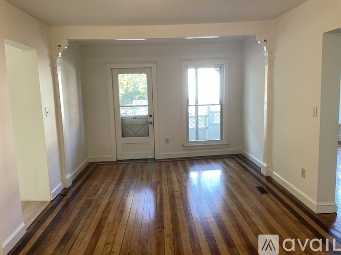 A room with wooden floors and white walls, with a door and a window.