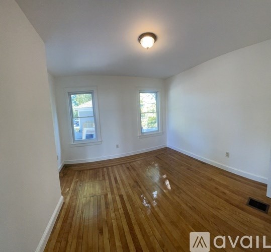 A room with wooden flooring and two windows.