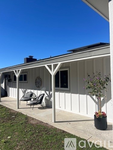 A white house with a porch and a tree in a planter.