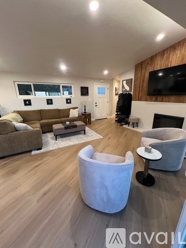 A living room with a brown couch, a white chair, and a television mounted on the wall.