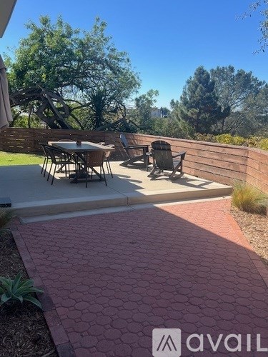 A patio with a table and chairs is surrounded by a brick walkway and a wooden fence.