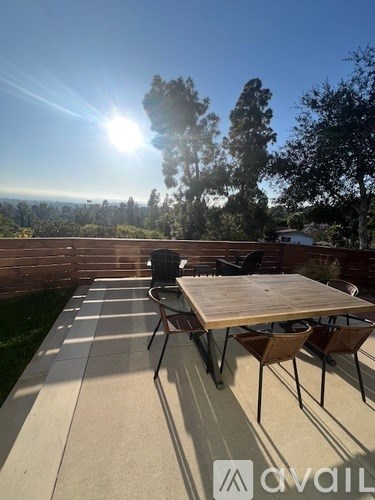 A table and chairs are set up on a patio with a view of the trees and mountains.
